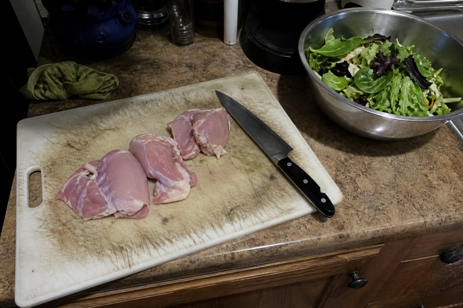 Raw chicken on a scratched plastic cutting board next to salad