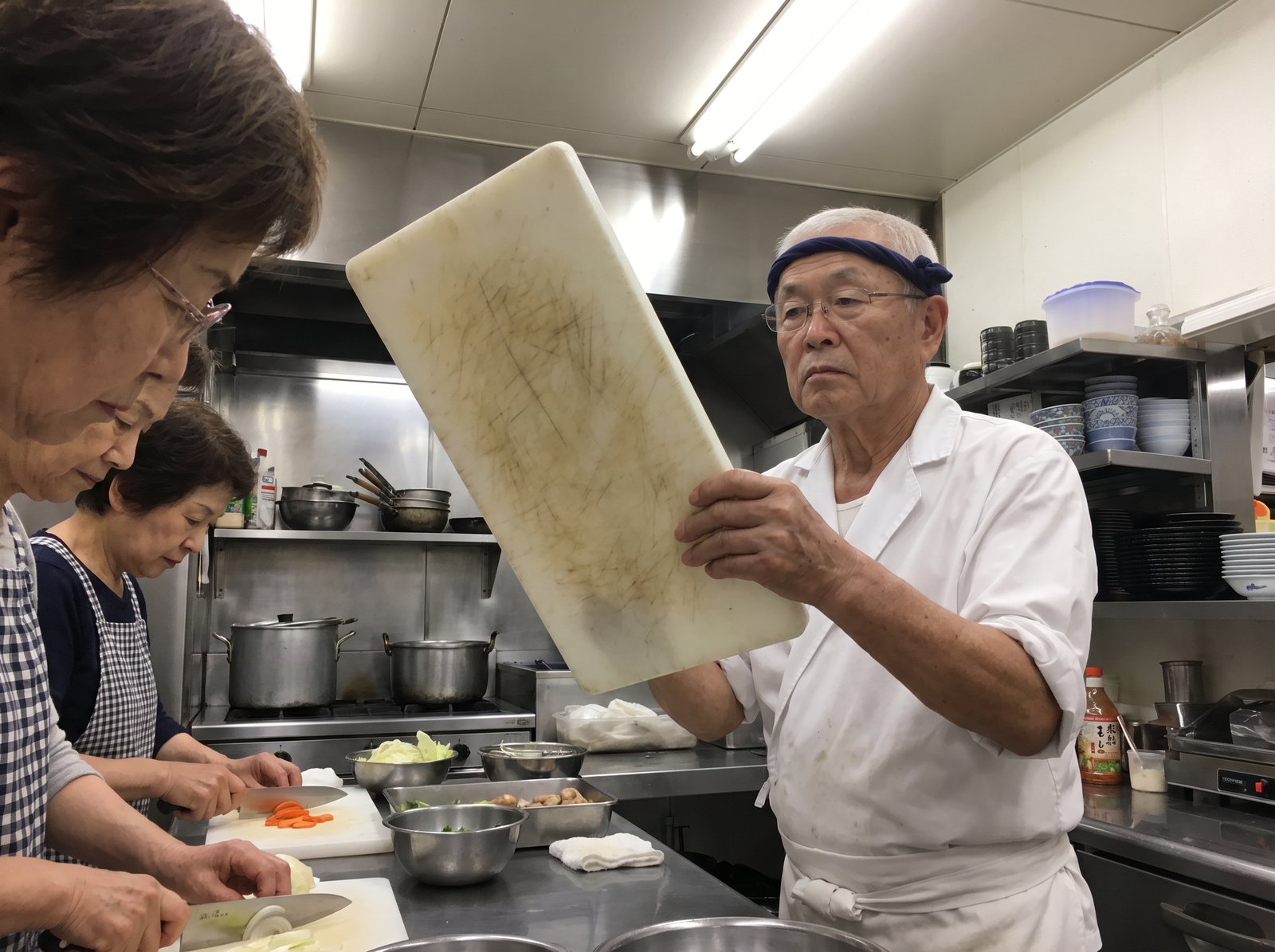 Chef Kenji Morita holding up a scratched plastic cutting board in his restaurant kitchen