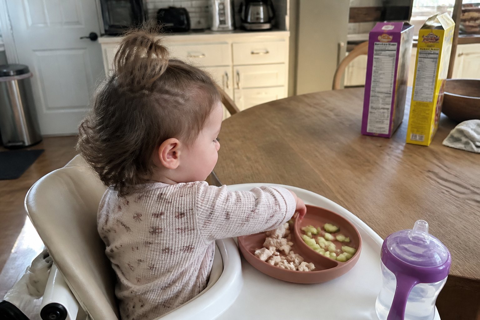 A toddler eating diced chicken and cucumber from a plate