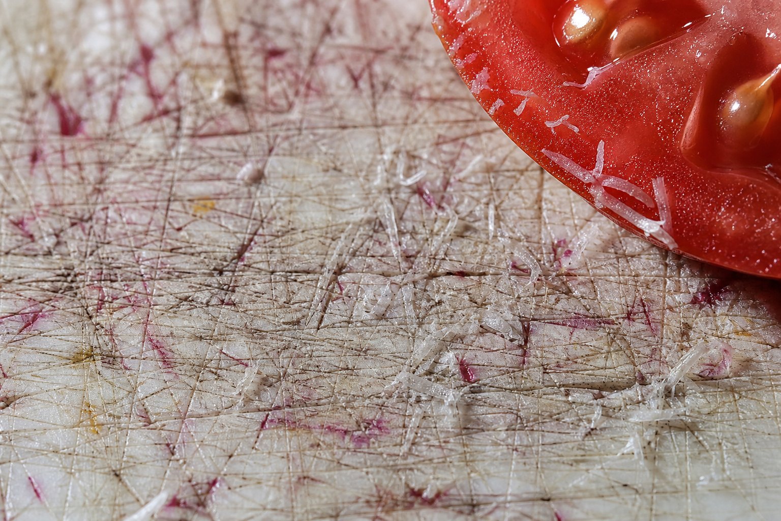 Close-up of knife grooves and plastic shavings on a white plastic cutting board